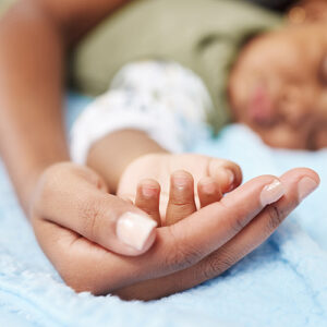 A close-up of a child's hand resting in an adult's hand, both lying on a soft blue surface.